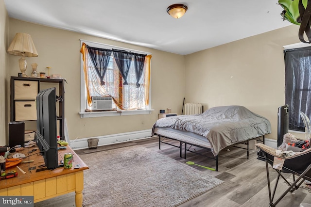 bedroom featuring cooling unit, radiator, baseboards, and wood finished floors