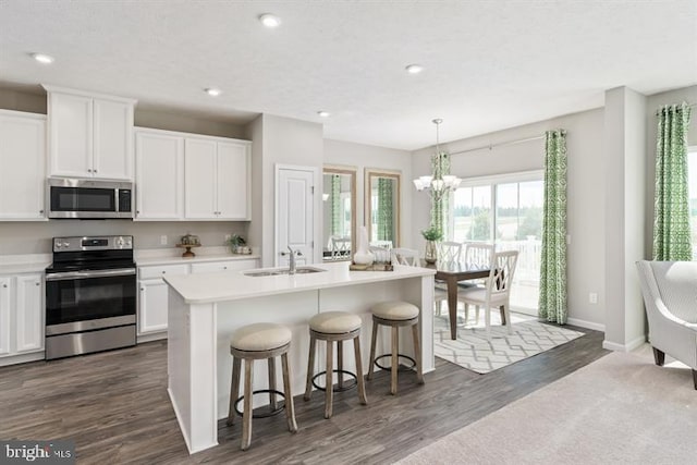 kitchen with stainless steel appliances, sink, white cabinets, dark hardwood / wood-style floors, and an island with sink