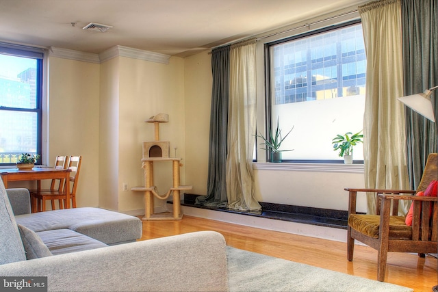 living area with baseboards, ornamental molding, visible vents, and light wood-style floors