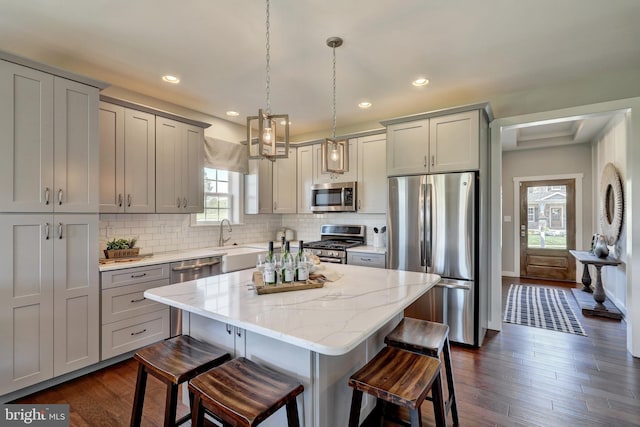 kitchen with light stone counters, a kitchen breakfast bar, a kitchen island, decorative light fixtures, and stainless steel appliances