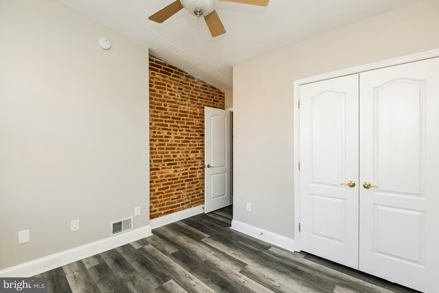 unfurnished bedroom with ceiling fan, brick wall, dark wood-type flooring, and lofted ceiling