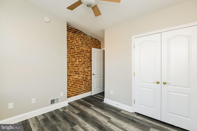 unfurnished bedroom featuring dark wood finished floors, visible vents, vaulted ceiling, brick wall, and baseboards