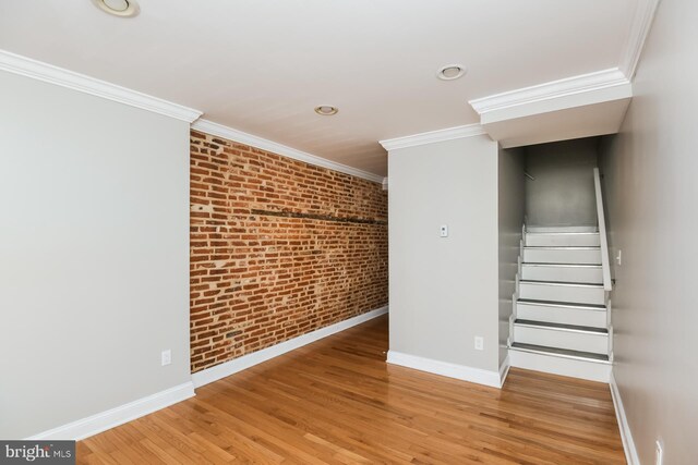 interior space featuring hardwood / wood-style floors, ornamental molding, and brick wall