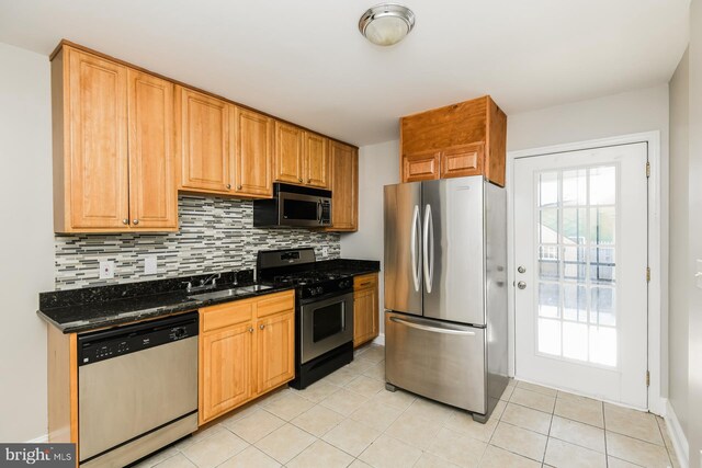 kitchen featuring backsplash, sink, dark stone countertops, appliances with stainless steel finishes, and light tile patterned floors