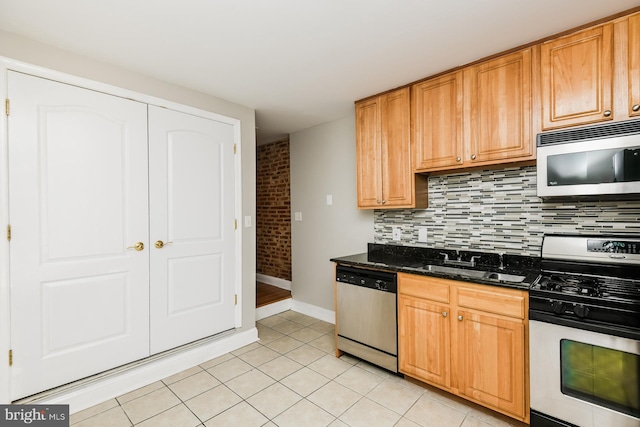 kitchen featuring stainless steel appliances, backsplash, light tile patterned flooring, a sink, and dark stone countertops