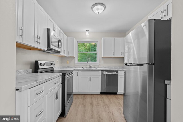 kitchen with stainless steel appliances, light hardwood / wood-style floors, sink, light stone counters, and white cabinets