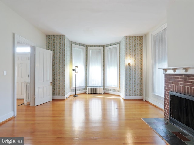 living room featuring light wood-type flooring, radiator, and a brick fireplace