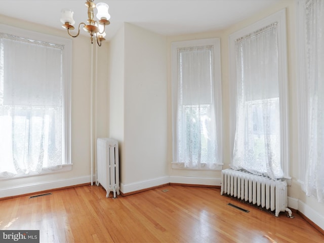 unfurnished room featuring a wealth of natural light, radiator heating unit, and light wood-type flooring