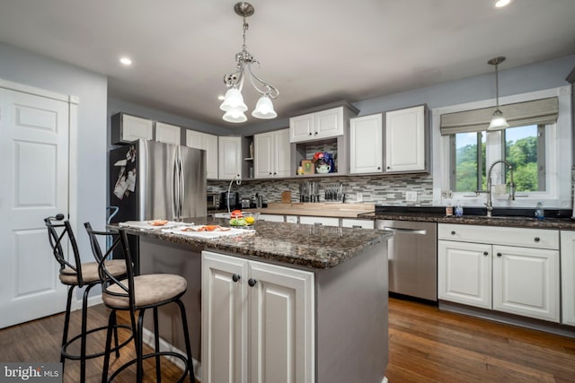 kitchen with appliances with stainless steel finishes, sink, white cabinets, a kitchen island, and dark wood-type flooring