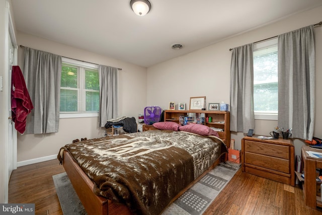 bedroom with multiple windows, dark wood finished floors, visible vents, and baseboards