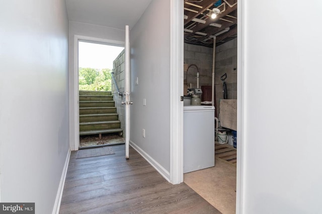 corridor with concrete block wall, baseboards, washer / clothes dryer, wood finished floors, and stairs