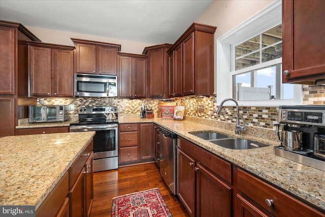 kitchen with tasteful backsplash, dark wood finished floors, light stone counters, stainless steel appliances, and a sink