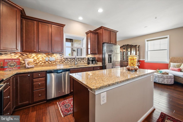 kitchen featuring dark wood-style flooring, a sink, a center island, appliances with stainless steel finishes, and light stone countertops