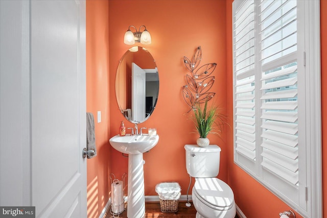 half bath featuring toilet, baseboards, and a sink