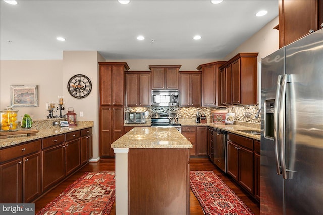 kitchen featuring light stone counters, a center island, stainless steel appliances, decorative backsplash, and dark wood-type flooring