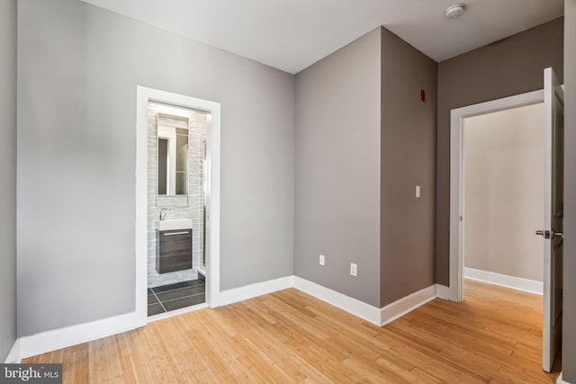 unfurnished bedroom featuring sink, connected bathroom, and hardwood / wood-style flooring