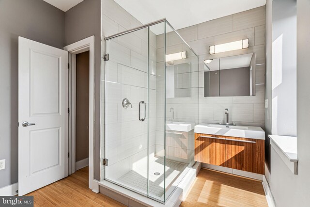 bathroom with hardwood / wood-style flooring, a shower with door, vanity, and tile walls