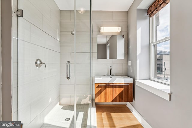 bathroom with hardwood / wood-style flooring, tile walls, a shower with shower door, and vanity