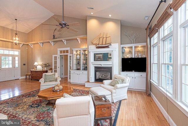 living room featuring ceiling fan, light hardwood / wood-style flooring, high vaulted ceiling, and built in shelves