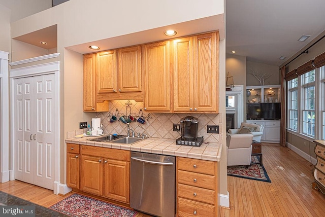 kitchen featuring dishwasher, tile countertops, lofted ceiling, light wood-style floors, and a sink