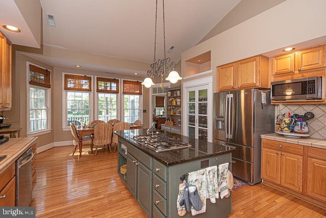 kitchen featuring light wood-type flooring, decorative backsplash, a kitchen island, stainless steel appliances, and pendant lighting