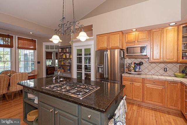 kitchen featuring dark stone countertops, appliances with stainless steel finishes, glass insert cabinets, and a kitchen island with sink