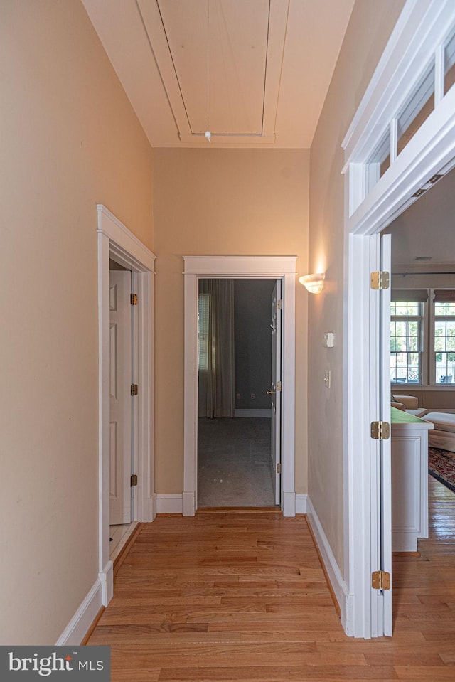 hallway with light wood finished floors, attic access, and baseboards