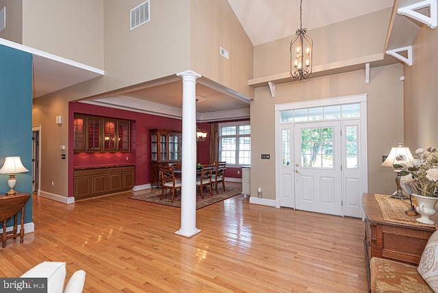 entryway featuring light wood-type flooring, a towering ceiling, decorative columns, and an inviting chandelier