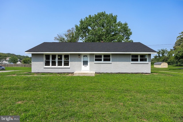 ranch-style home featuring a storage unit, a front lawn, fence, and brick siding