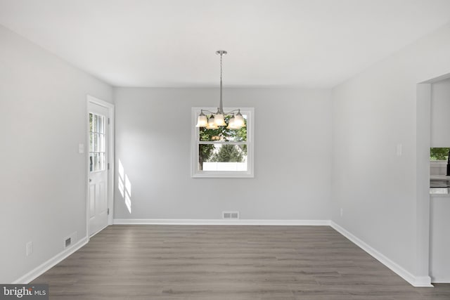 unfurnished dining area featuring dark wood-type flooring, visible vents, baseboards, and an inviting chandelier