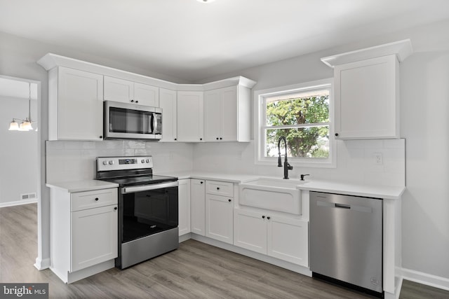 kitchen with stainless steel appliances, a sink, white cabinets, light countertops, and tasteful backsplash