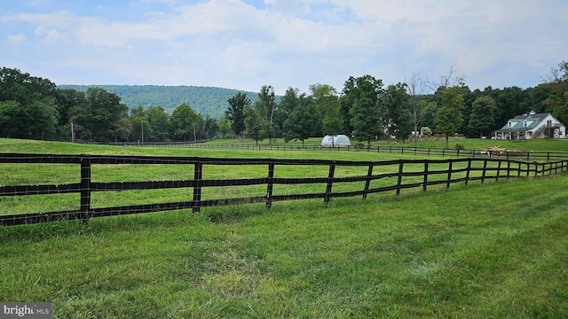 view of yard with a rural view, fence, a view of trees, and a mountain view