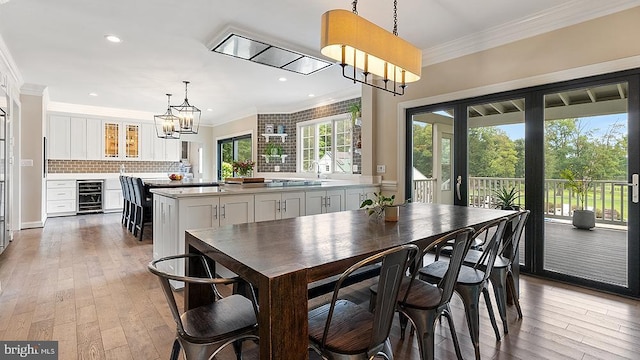 dining room featuring light wood finished floors, wine cooler, and crown molding