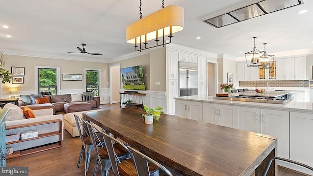 dining space with ornamental molding, ceiling fan with notable chandelier, and wood finished floors