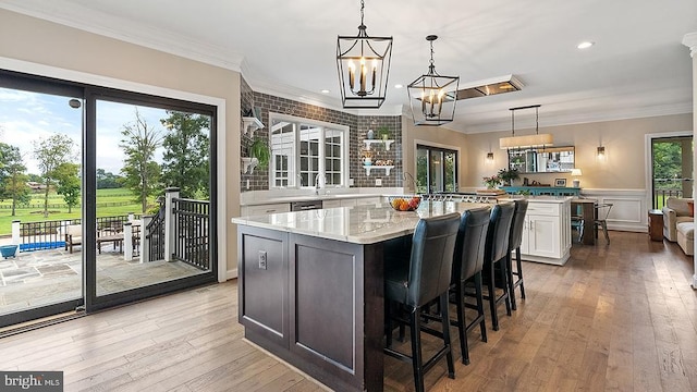 kitchen with crown molding, a kitchen island, white cabinetry, light wood-style floors, and pendant lighting