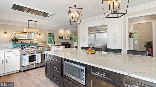 kitchen with crown molding, a fireplace, white cabinetry, built in appliances, and a chandelier