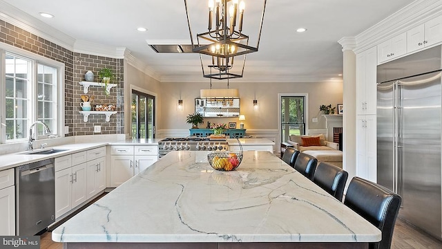 kitchen featuring stainless steel appliances, ornamental molding, a kitchen island, a sink, and light stone countertops