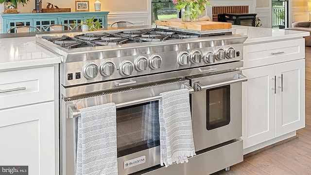 room details featuring white cabinets, range with two ovens, a wainscoted wall, light wood-style floors, and a decorative wall