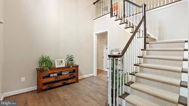 entrance foyer with stairway, a towering ceiling, baseboards, and wood finished floors