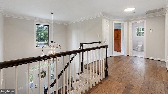 hallway with visible vents, hardwood / wood-style floors, an inviting chandelier, crown molding, and an upstairs landing