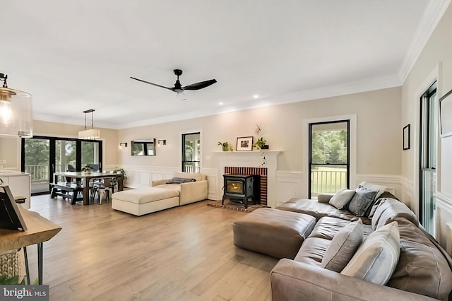 living room with a fireplace, a wood stove, light hardwood / wood-style floors, ornamental molding, and ceiling fan