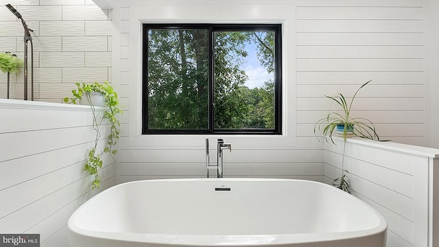 full bath featuring a soaking tub, a healthy amount of sunlight, and wood walls