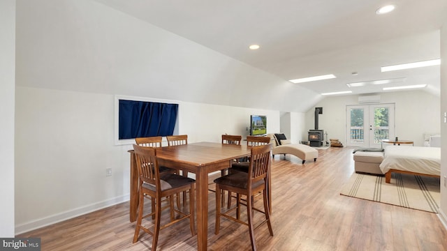 dining area featuring light wood finished floors, baseboards, a wall mounted air conditioner, a wood stove, and vaulted ceiling