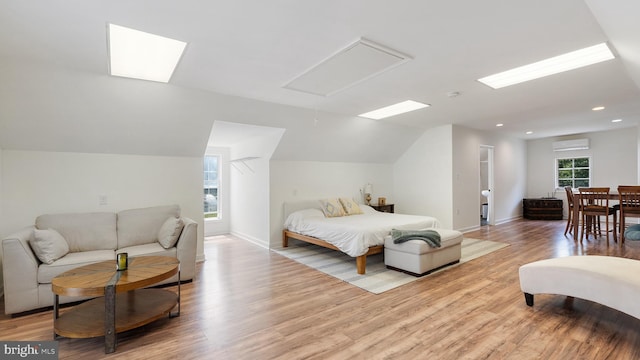 bedroom with vaulted ceiling, light wood-style flooring, baseboards, and a wall mounted AC