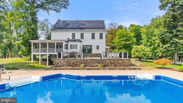 rear view of property with a sunroom, an outdoor pool, solar panels, and a patio