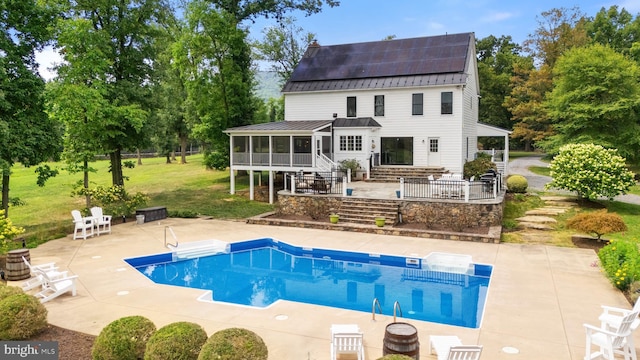 back of house with a lawn, a patio, a sunroom, a standing seam roof, and roof mounted solar panels