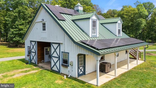 view of barn with solar panels, a lawn, and central AC