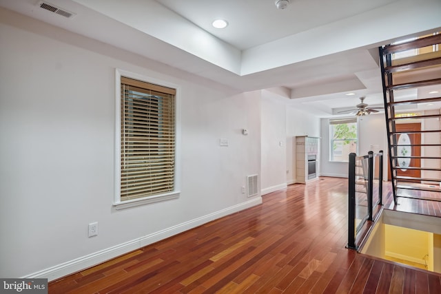 empty room with a ceiling fan, wood finished floors, visible vents, and baseboards