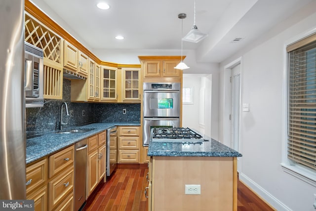 kitchen with decorative light fixtures, a kitchen island, a sink, appliances with stainless steel finishes, and glass insert cabinets