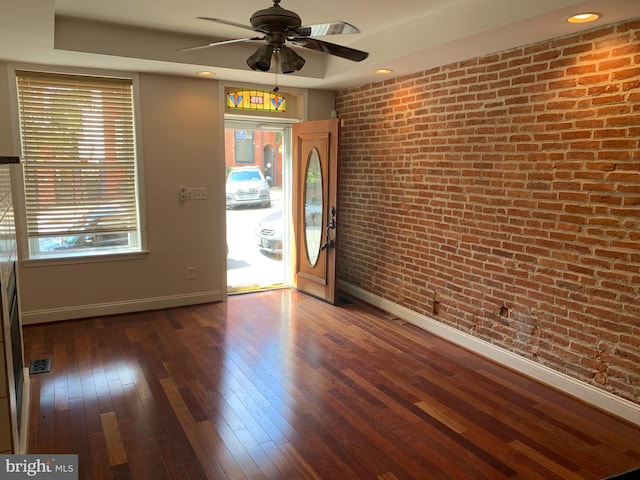 spare room with ceiling fan, dark hardwood / wood-style floors, brick wall, and a tray ceiling